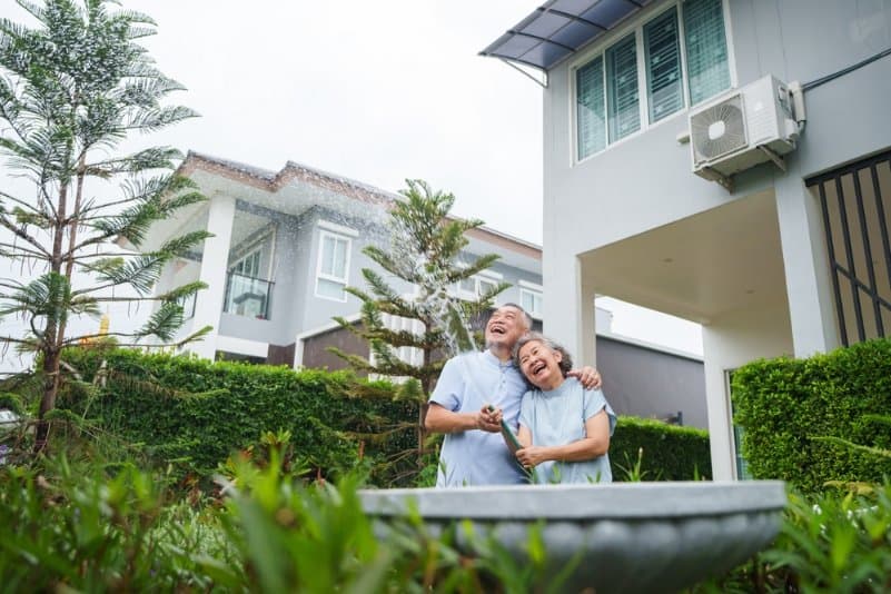 คุณตาคุณยายยืนอยู่หน้าบ้านที่ได้รับการออกแบบมาเพื่อผู้สูงอายุโดยเฉพาะ